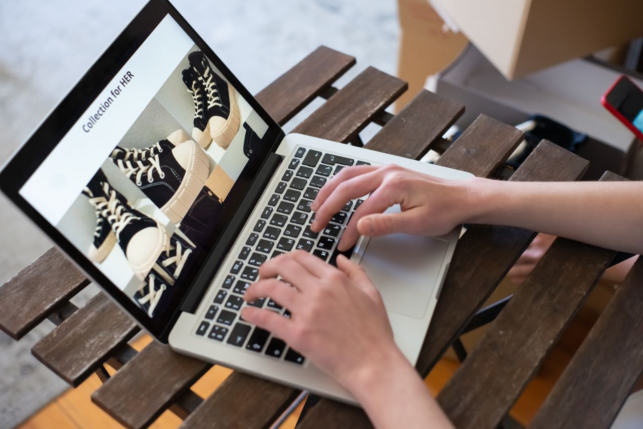 brand-01 Hands of a person browsing a Collection for HER on an online shoe store using a laptop.